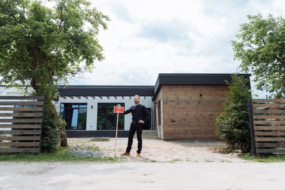 actualité immobilier france — Agent immobilier se tenant dehors d'une maison moderne avec un panneau à vendre, affichant un